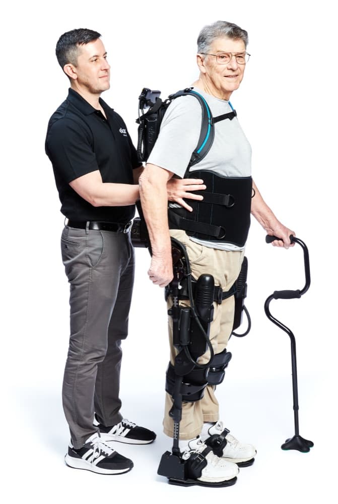 A rehabilitation exoskeleton (Ekso Bionics EksoNR) helping a man walk with a therapist's support